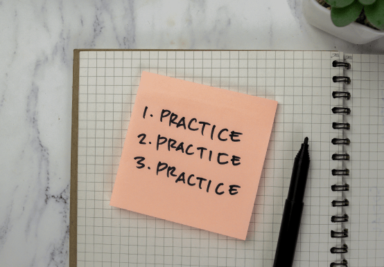 Grid lined notepad with small not saying 1. practice 2. practice 3. practice and a black pen to the right 